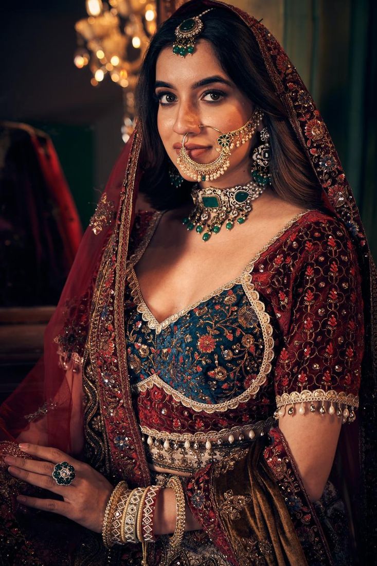 Bride in a maroon velvet lehenga with emerald kundan choker, nath and maang tikka